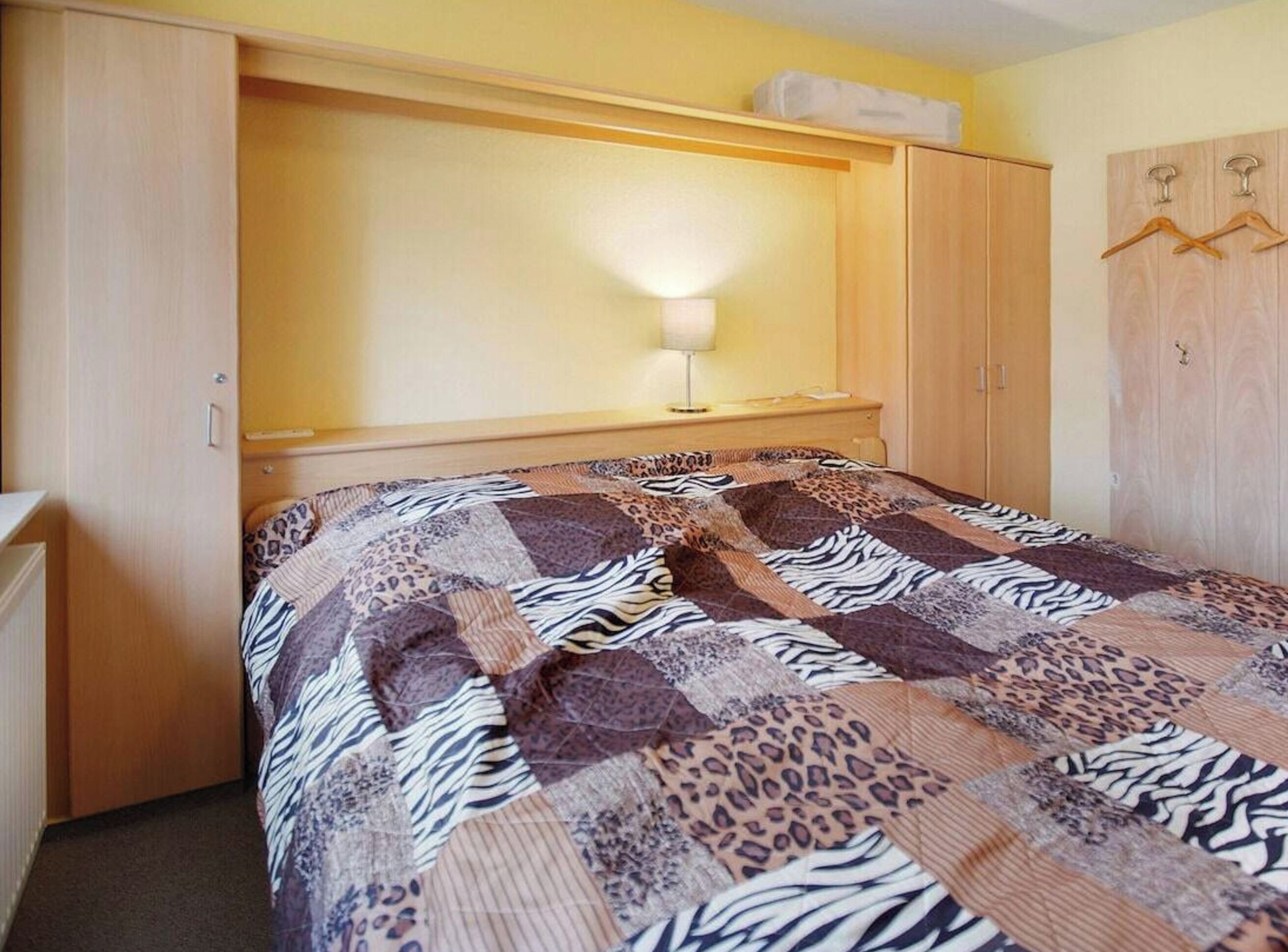 Ein Einzelbett mit einer Zebra-Decke, eine Nachttischlampe und ein Holzschrank mit Kleiderhaken.
