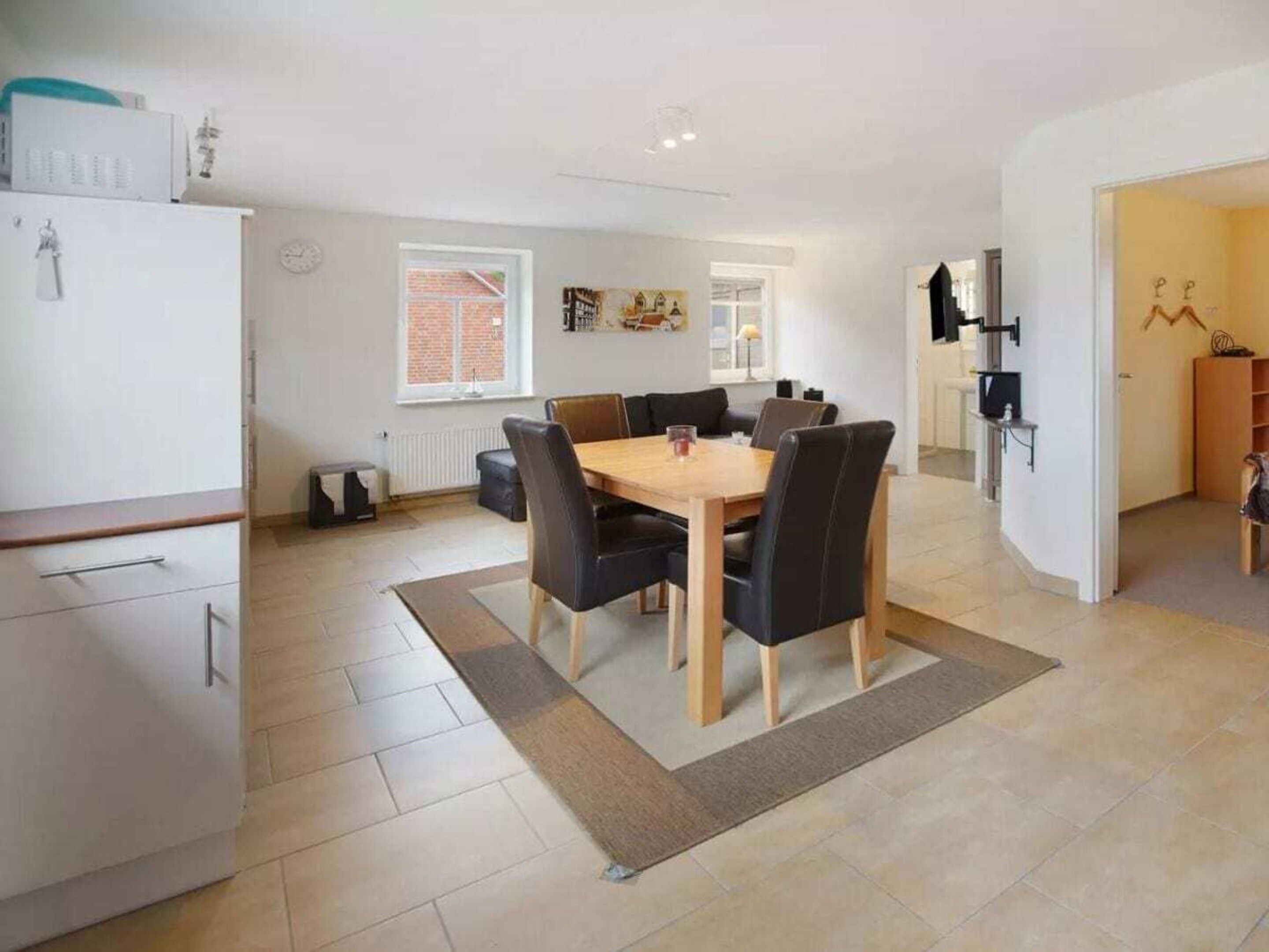 A modern kitchen with a white refrigerator, a dining area with a wooden table and black chairs, and a visible window with a view of a brick wall.
