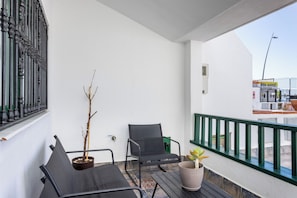 A balcony with a black chair, a potted plant, and a view of a building with a sign. - Home2Book Family House, Pool & Garage (Puerto Santiago)