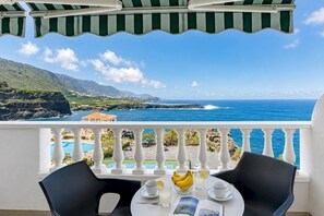 Ein Balkon mit Blick auf das Meer und ein Berg, ein Tisch mit einer Bananenschale, Tassen und einem Glas.