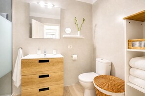 Ein modernes Badezimmer mit einem Holzwaschtisch, einer Toilette, einem Spiegel und einem Korbwäscheschrank.