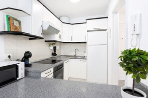 Una cocina moderna con armarios blancos, encimera negra, horno empotrado y cafetera.