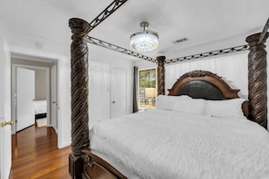 Ein Himmelbett mit einer Chandelüster, Holzboden und eine Tür zu einem weiteren Raum.