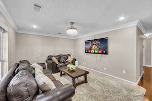 A living room with a sectional sofa, a coffee table, and a mounted TV displaying a movie poster. - Lovely 2-bedroom home in Royse City (royse city)