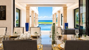 Un espace repas avec des tables dressées pour le dîner, donnant sur une piscine et offrant une vue sur l’océan.