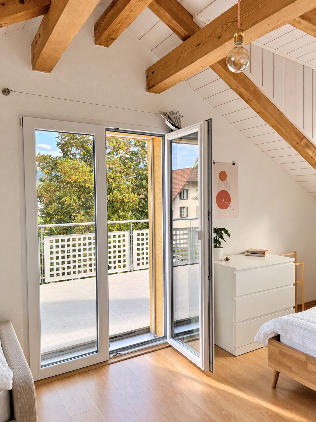 A bedroom with a sliding glass door leading to a balcony, a white dresser, a bed, and a hanging light fixture.