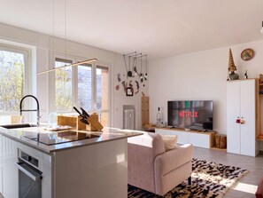 A modern kitchen with a central island, a dining area with a sofa, a TV, and a cabinet. - Casa Cenni Bright 2BR M1 Citylife (Milan)