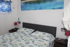 Ein Schlafzimmer mit einem Bett, einem Nachttisch, einer Lampe und einem Wandbild.