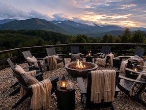 Ein Außenbereich mit Lounge-Möbeln und einem zentralen Feuerkorb, umgeben von Kieselsteinen und mit Blick auf eine gebirgige Landschaft.