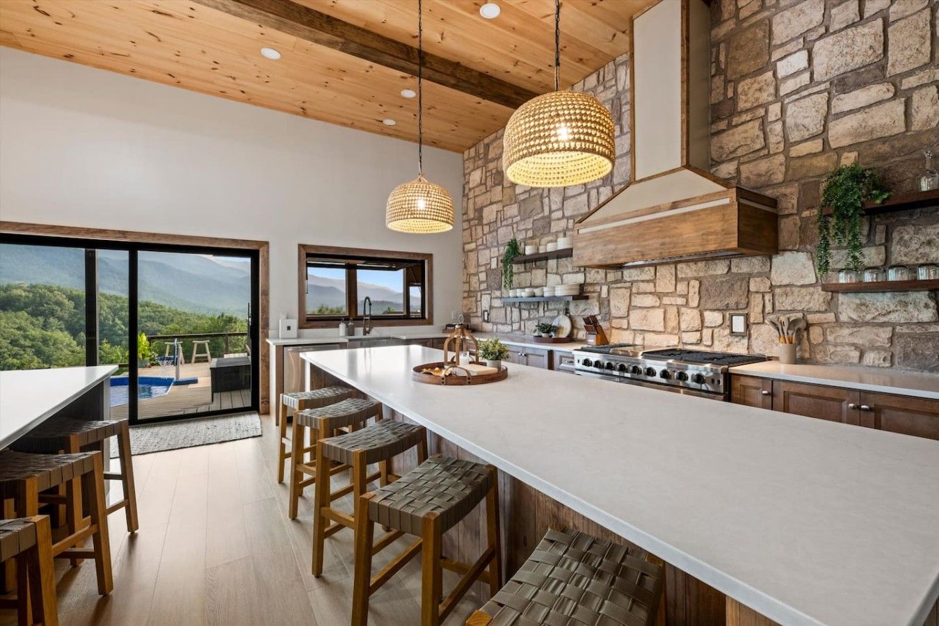 Une cuisine moderne dotée d’un grand îlot central, d’un mur recouvert de pierres apparentes et offrant une vue sur un paysage montagneux.