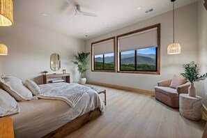 Ein modernes Schlafzimmer mit Bett, Sessel, Schreibtisch und einem großen Fenster mit Blick auf die Berge.