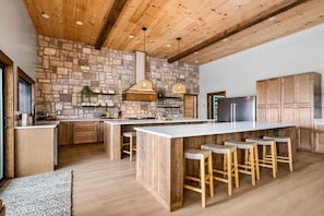 Eine moderne Küche mit einer großen Kochinsel, Holzbarhocker und einer Wand mit Steinverkleidung.