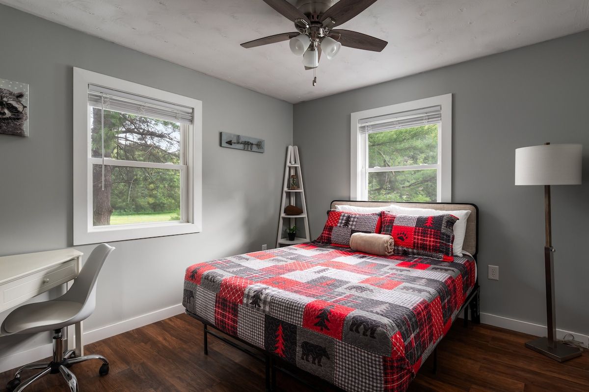 Un dormitorio con cama, escritorio, silla, escalera y lámpara de pie.