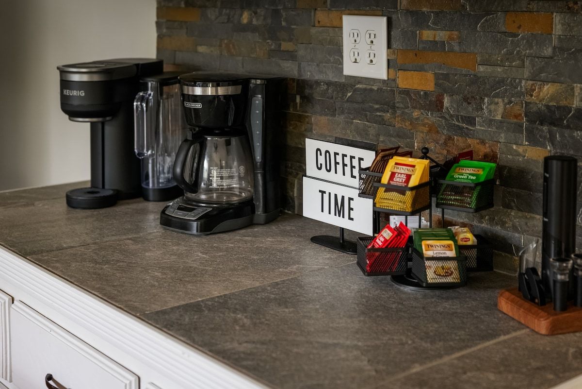 Un coin café équipé d’une machine Keurig, d’une cafetière, ainsi que de boîtes de thé et de café de la marque Twinings.