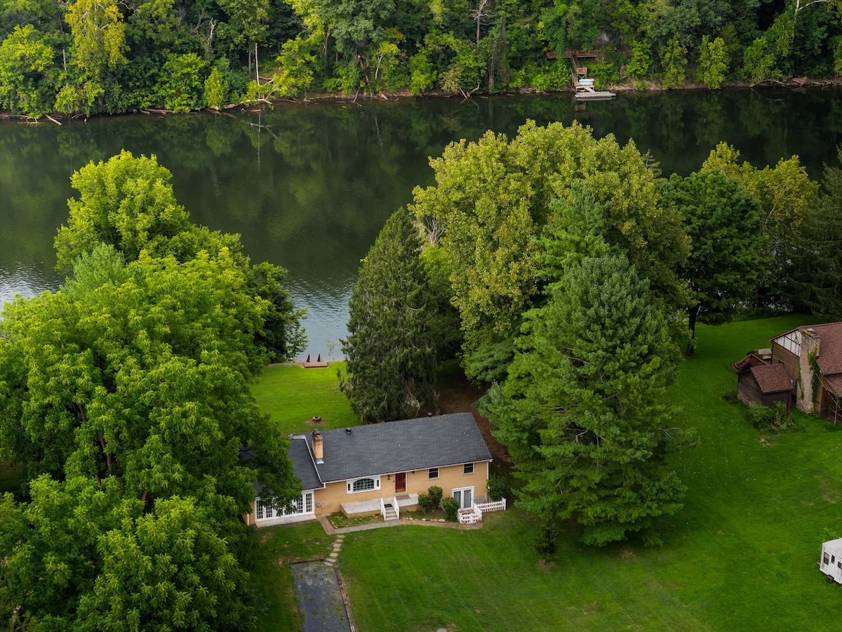 Una casa con césped, un muelle y árboles junto a un lago.