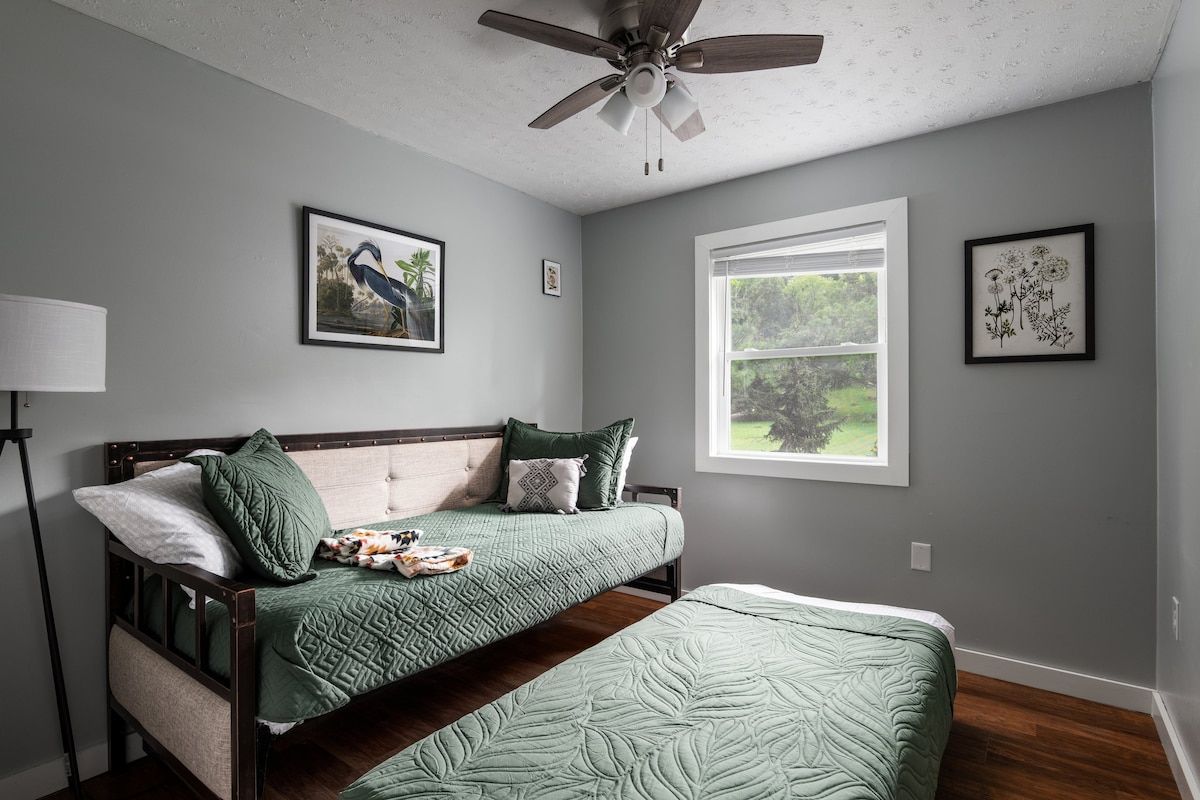 A bedroom with a bed, a ceiling fan, a window, and wall art.