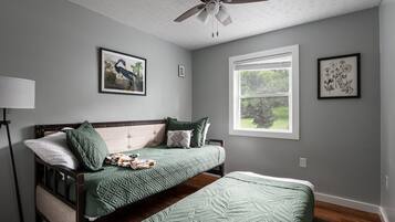 A bedroom with a bed, a ceiling fan, a window, and wall art.