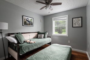 A bedroom with a bed, a ceiling fan, a window, and wall art.