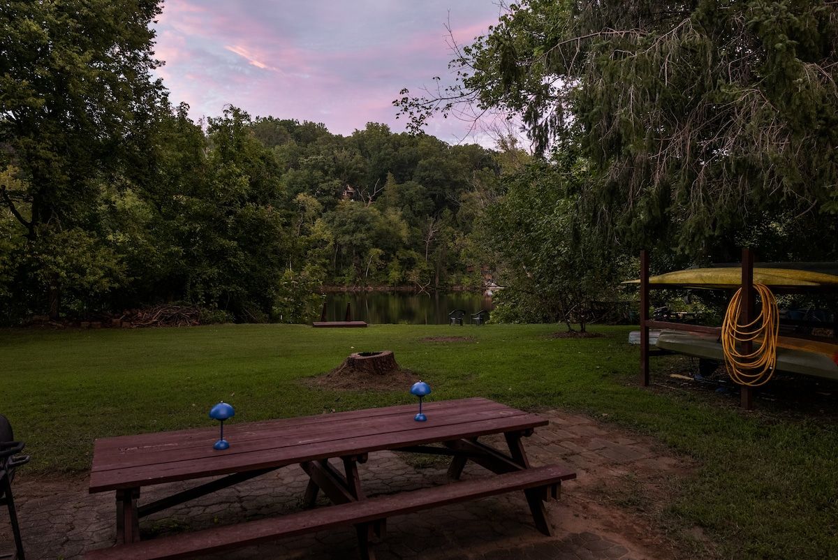 Una mesa de picnic con dos lámparas azules, rodeada de un césped con árboles y un lago al fondo.