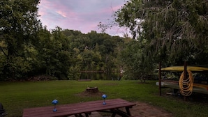 Taula de picnic amb dues làmpades blaves, envoltada per una zona verda amb arbres i un llac al fons.