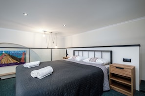 Moderni hotellihuone, jossa on suuri sänky, yöpöytä, yövalaisin ja taulu seinällä.