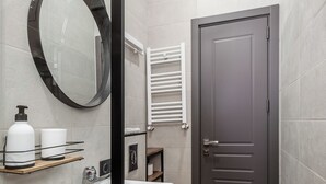 A modern bathroom with a wooden vanity, a large mirror, a toilet, and a door. - Lumina Apartment #8 (T'bilisi)