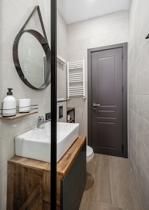 Un baño moderno con un tocador de madera, un espejo grande, un inodoro y una puerta.