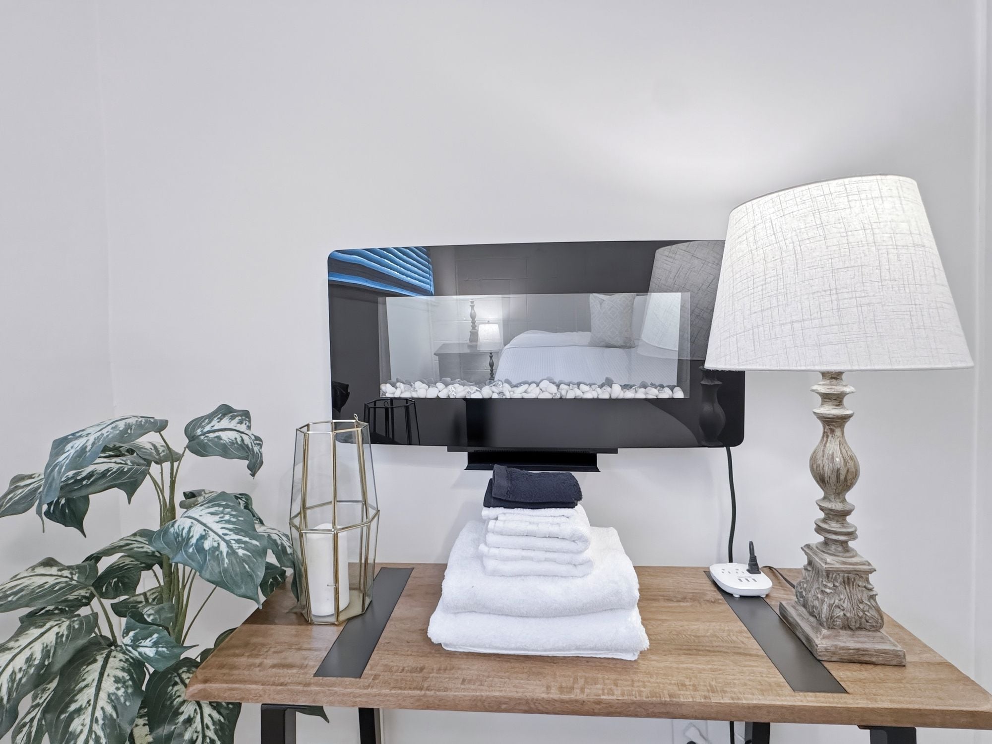 A hotel room with a bed, a television mounted on the wall, a lamp, a table with towels, and a plant.