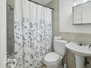 A bathroom with a shower curtain, toilet, sink, and a towel rack.
