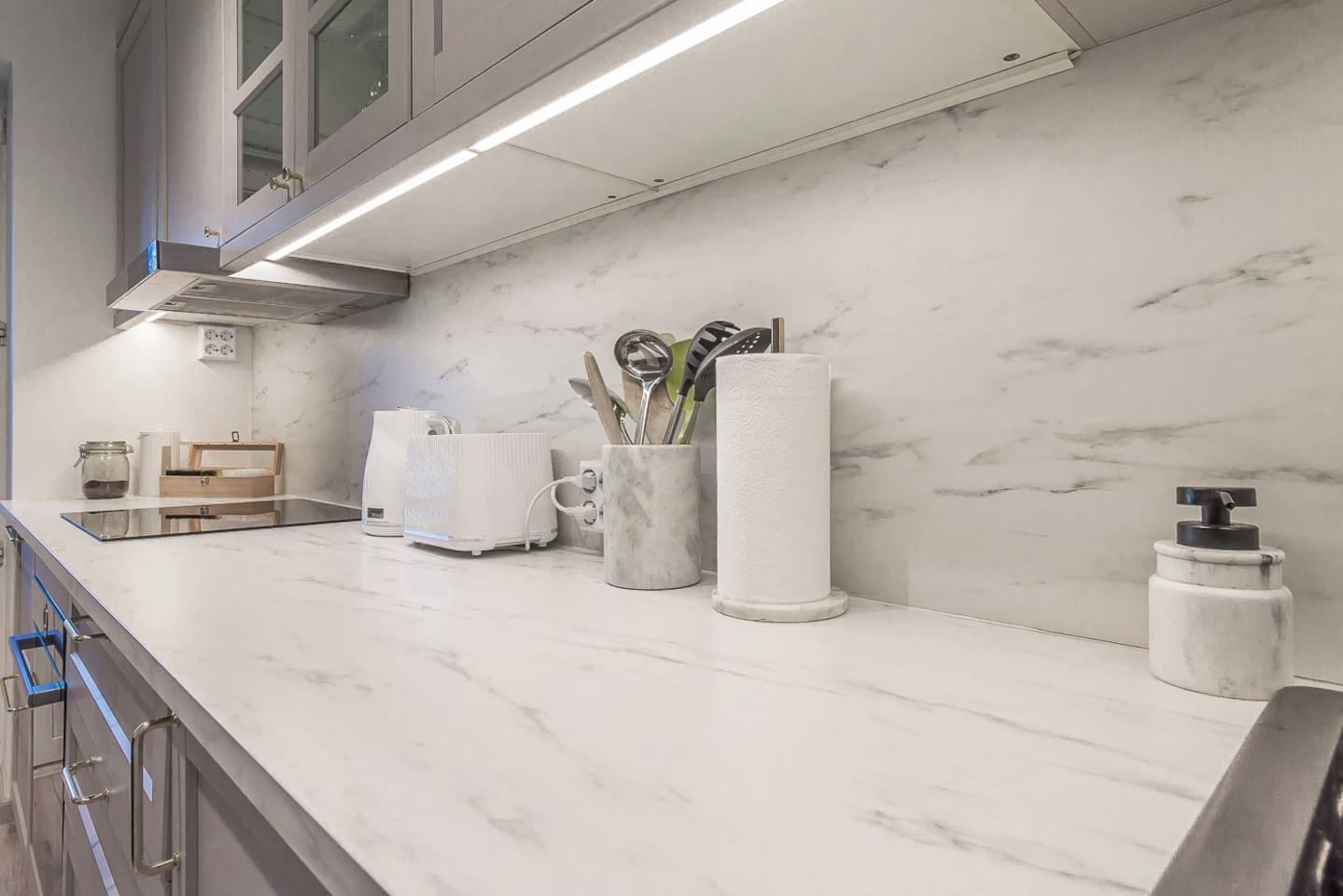 A kitchen with a marble countertop, a coffee maker, a paper towel dispenser, and a soap dispenser.