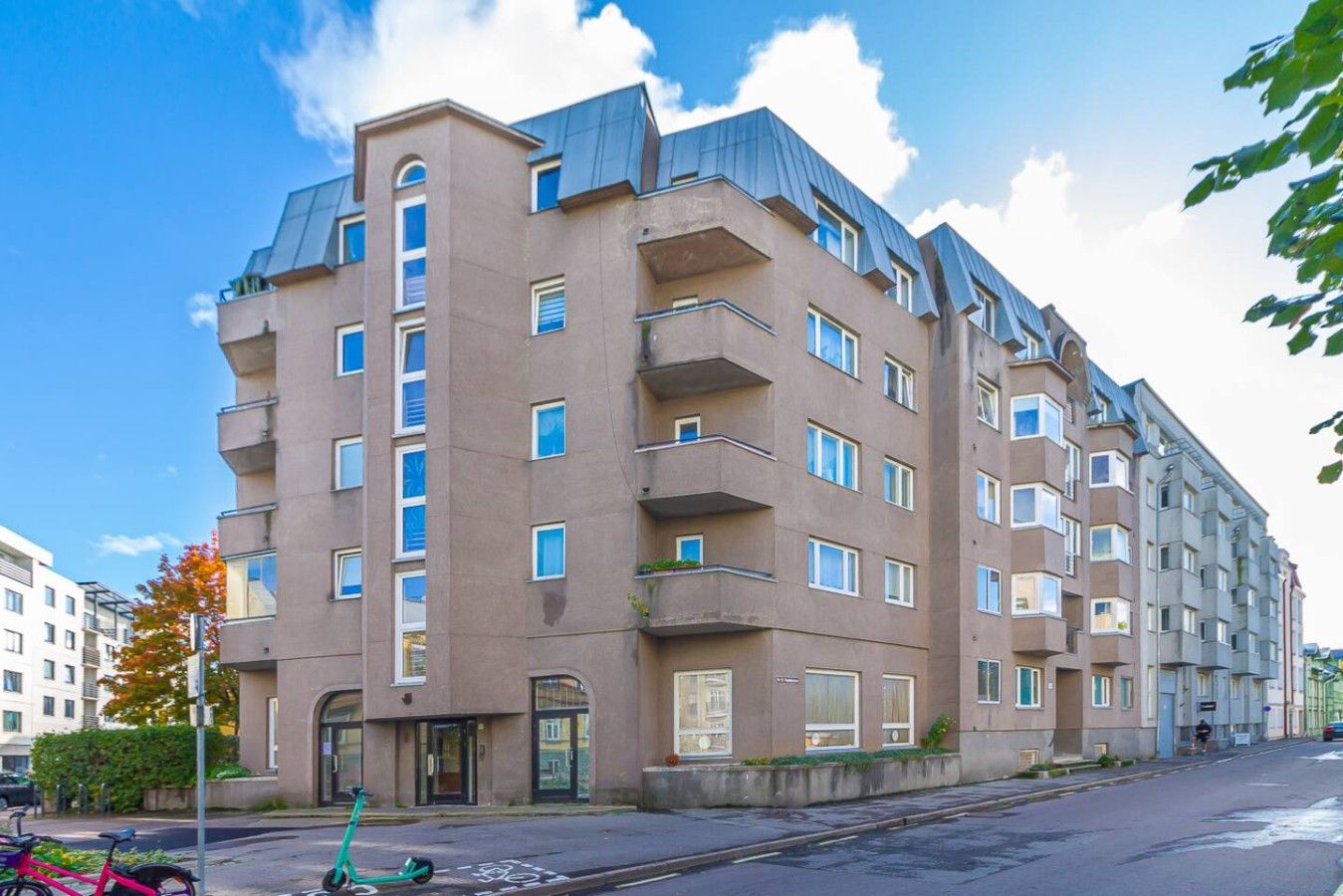 A multi-story residential building with balconies, a bicycle parked in front, and a clear sky.