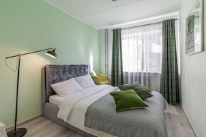 Ein Schlafzimmer mit einem Bett, einer Stehlampe und einem Fenster mit Vorhängen.