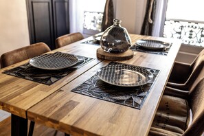 A wooden dining table with black placemats and a decorative glass vase. - Triplex Belle Époque | Hypercenter (Melun)