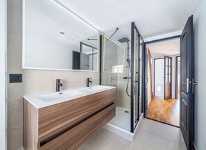 Ein modernes Badezimmer mit einem Doppelwaschbecken, einem großen Spiegel und einer Duschkabine.