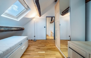 Ein Schlafzimmer mit Dachfenster, Holzboden, einem Bett, einem Nachttisch und einem Kleiderschrank.