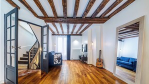Uma sala de estar ampla com piso de madeira, uma escada, um sofá azul, um violão e um espelho refletindo o ambiente.