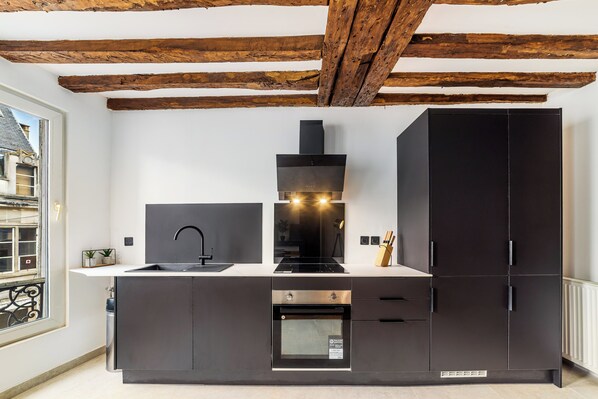 Une cuisine moderne avec des meubles de couleur sombre, un évier en acier inoxydable et un four encastré.