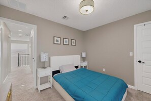 Un dormitorio con cama, mesitas de noche, lámpara, puerta y ventana.