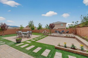 A backyard with a patio, outdoor furniture, a small garden, and a house in the background.