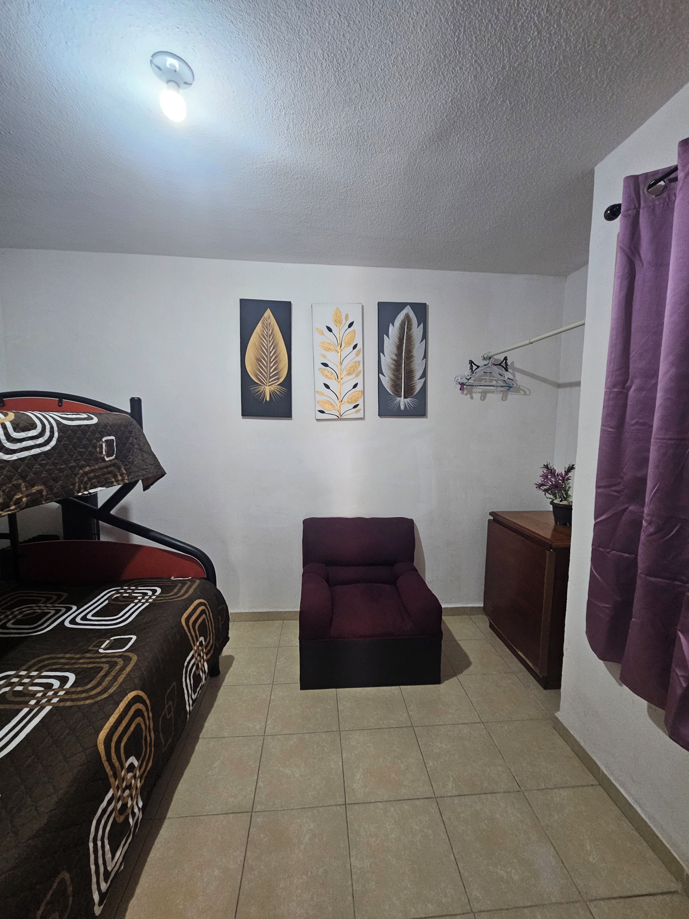 Quarto com cama, cadeira, mesinha e decoração na parede.