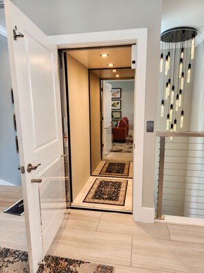 A hallway with a door leading to a room, a patterned rug on the floor, and a modern light fixture. - The Grand Mariner: Waterfront + Boat Slip + Elevator Luxury Estate (St. Augustine)