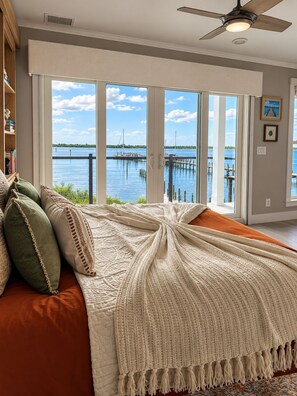 A bedroom with a large window, a bed with a white blanket, and a view of a body of water. - The Grand Mariner: Waterfront + Boat Slip + Elevator Luxury Estate (St. Augustine)