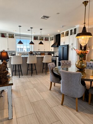 A modern kitchen with white cabinets, a central island, bar stools, and pendant lighting. - The Grand Mariner: Waterfront + Boat Slip + Elevator Luxury Estate (St. Augustine)