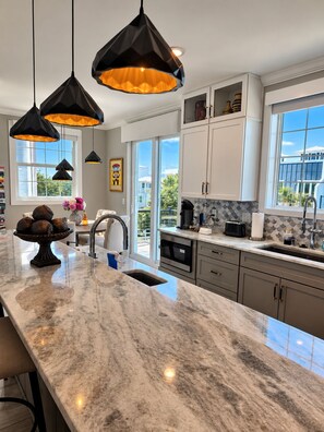 A modern kitchen with a marble countertop, pendant lights, and a view of the outside. - The Grand Mariner: Waterfront + Boat Slip + Elevator Luxury Estate (St. Augustine)