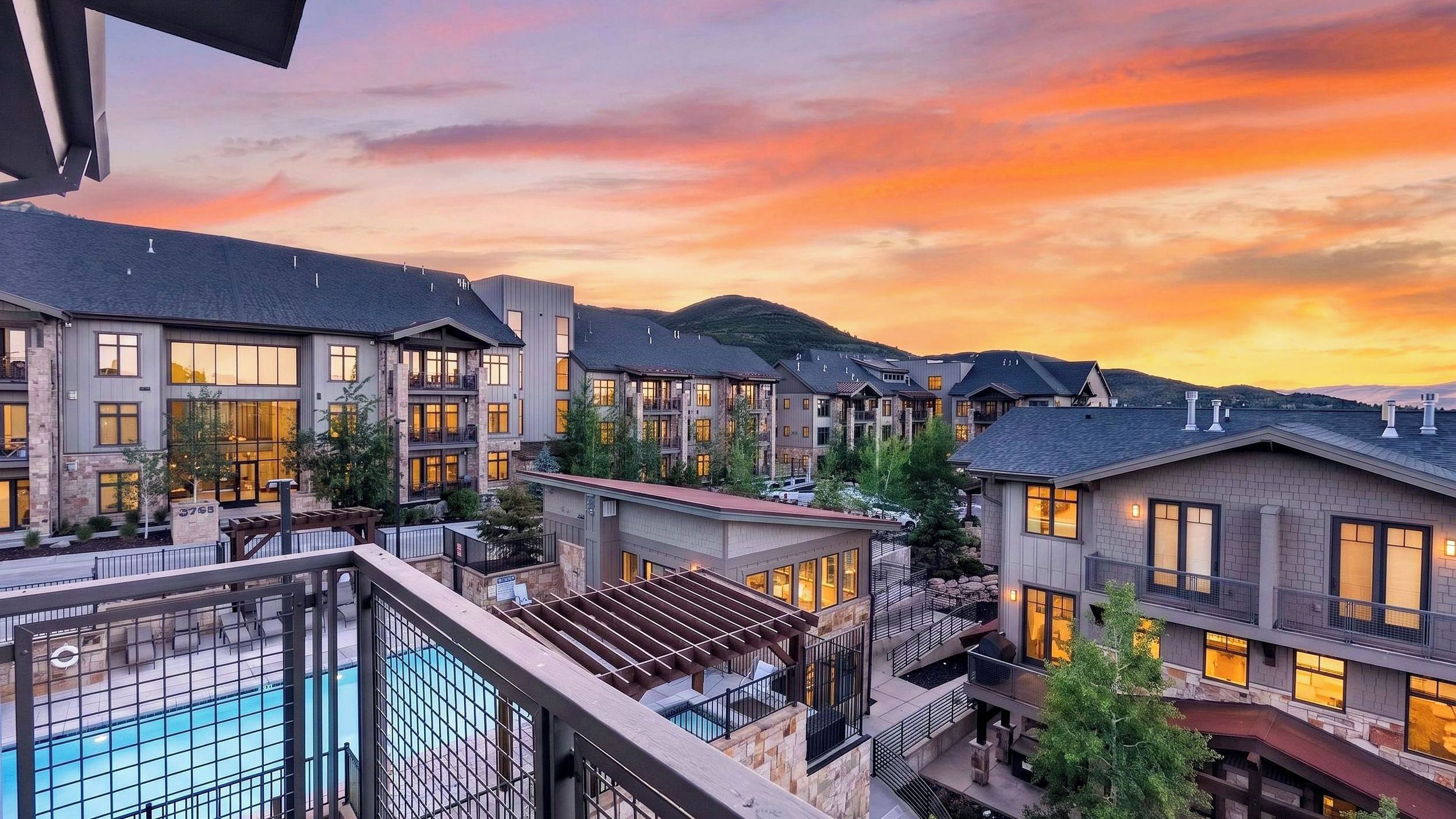A residential area with multiple two-story houses, a swimming pool, and a mountainous backdrop during sunset.
