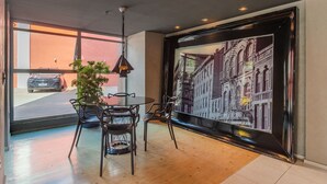 A modern interior with a dining area, a large window, and a cityscape mural. - Loft Praia #502 Loft With Sea View by Carpediem (Fortaleza)