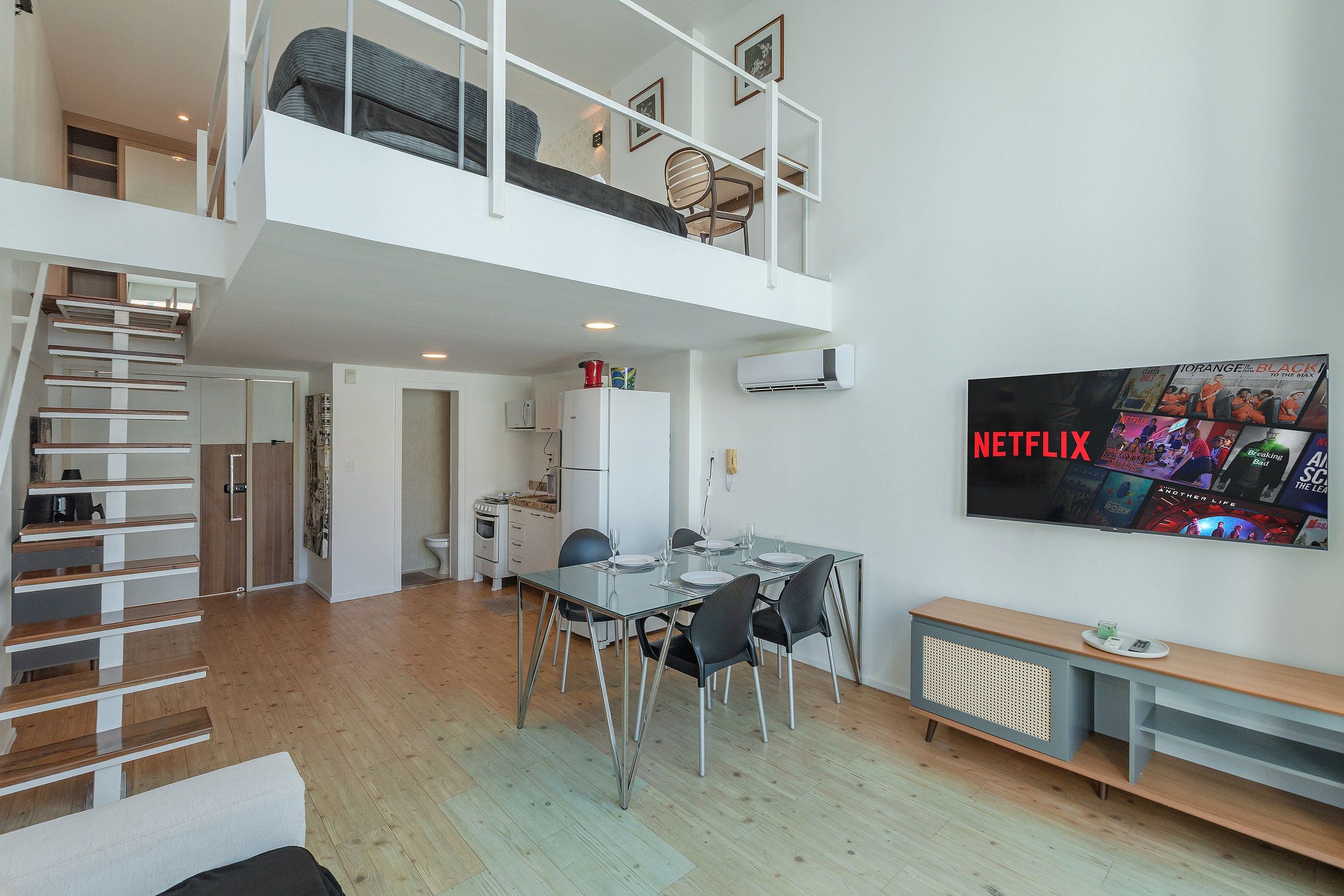 Un apartamento moderno con comedor, cocina y sala de estar con televisor montado en la pared.