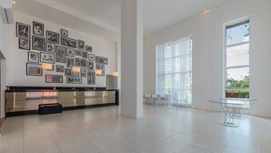 A spacious lobby with a long reception desk, a wall adorned with framed pictures, and a large window providing a view of the outdoors. - Loft Praia #502 Loft With Sea View by Carpediem (Fortaleza)
