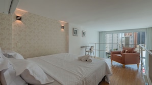 A hotel room with a bed, a chair, a desk, and a large window with a city view. - Loft Praia #502 Loft With Sea View by Carpediem (Fortaleza)
