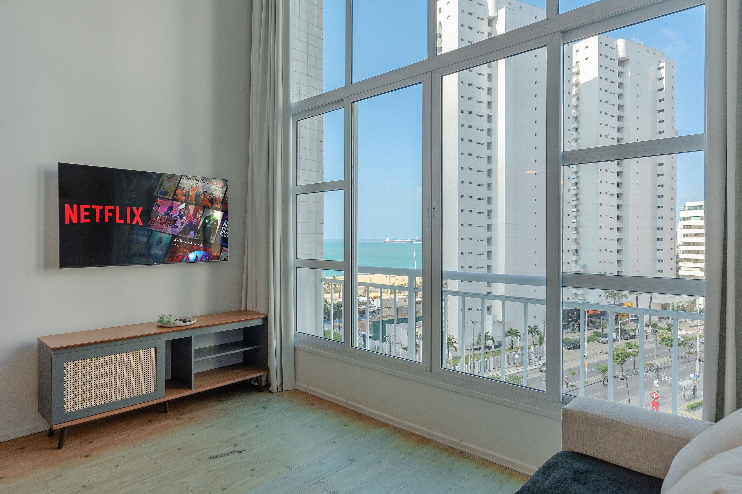 Una sala de estar moderna con un ventanal grande, un televisor de pantalla plana montado en la pared y un mueble de entretenimiento de madera.